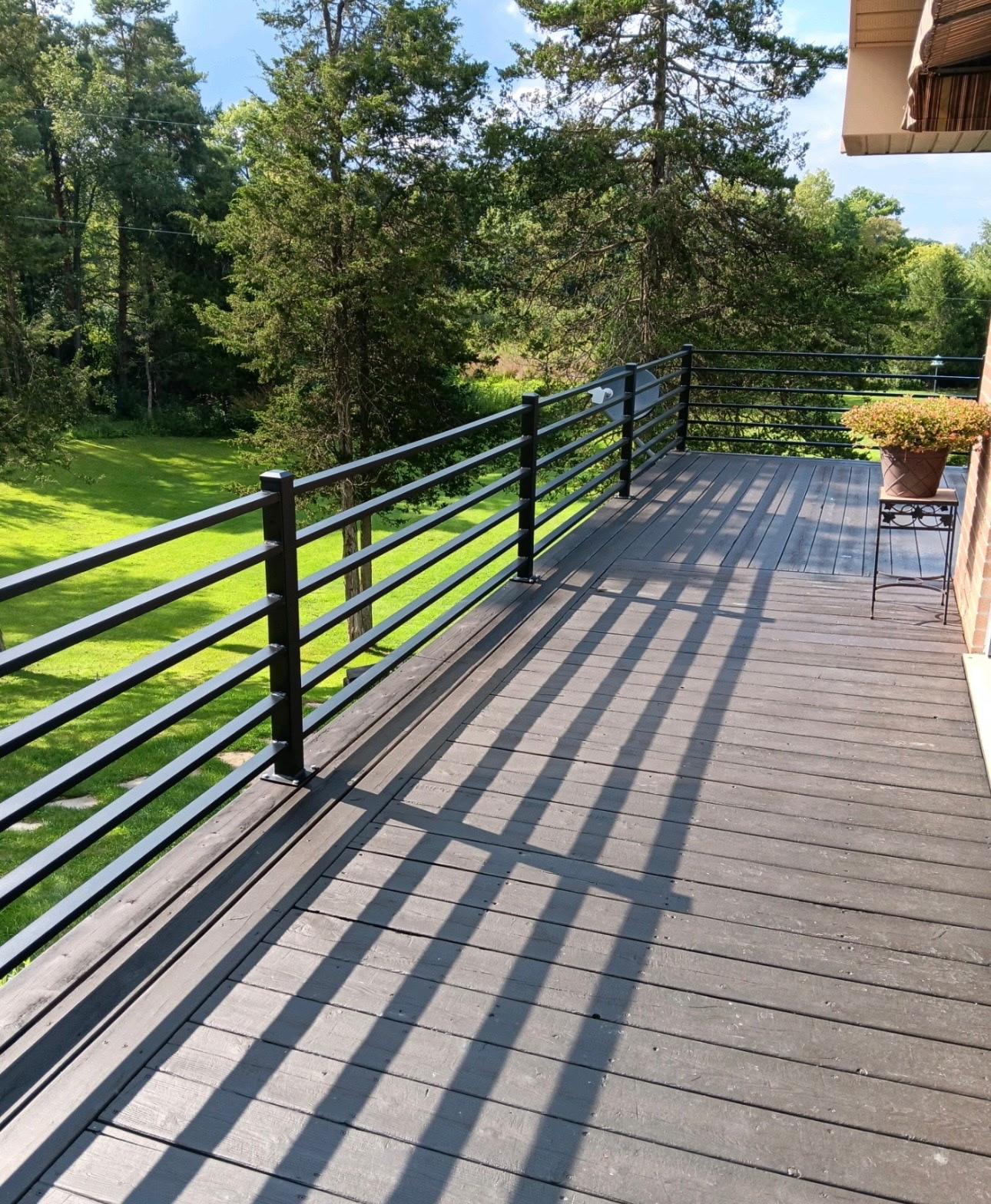 Composite deck with horizontal black aluminum railing overlooking wooded yard