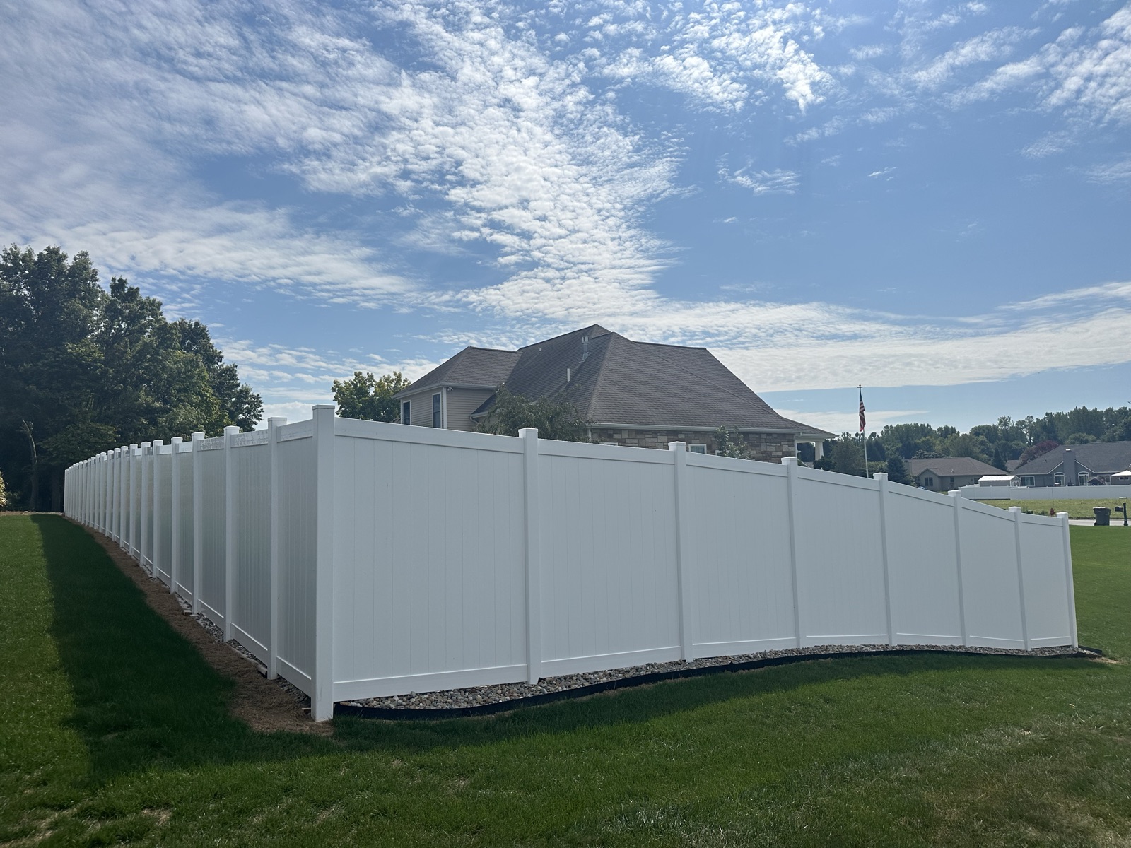 White vinyl privacy fence curving along a landscaped yard toward a stone and siding home in Warsaw, Indiana