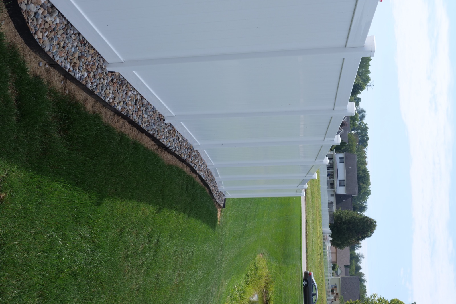 The finished 6-foot white vinyl privacy fence running along the property line, with the neighboring development visible beyond it