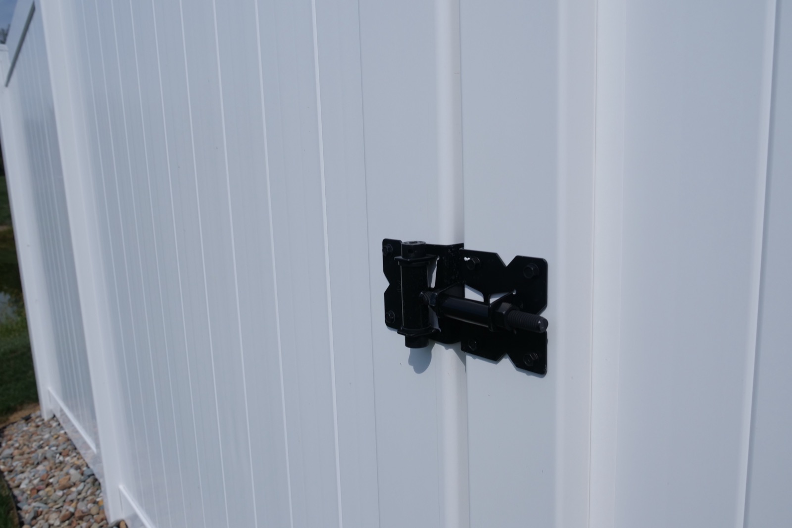Black self-latching gate hardware mounted on the white vinyl gate